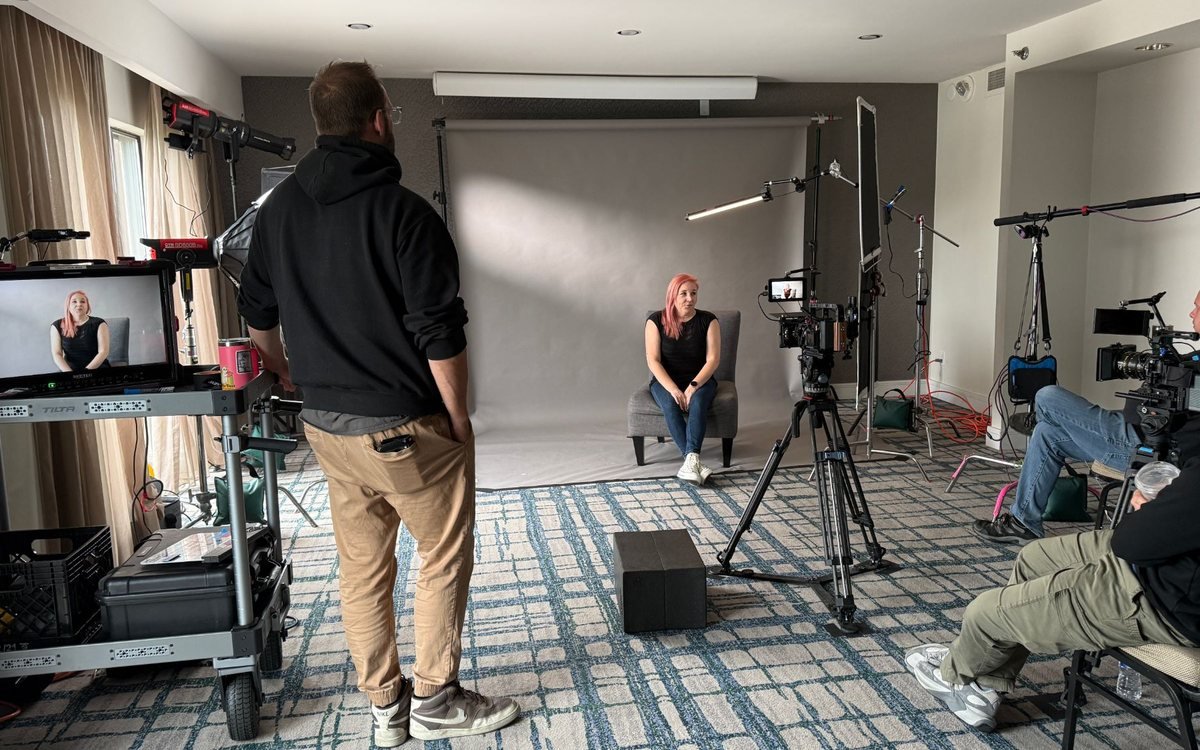 Volare Media crew filming a seated interview against a grey backdrop, the shot on the monitor cart